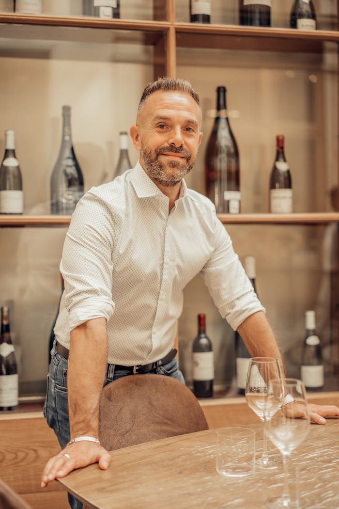 Smiling sommelier standing in a Paris wine bar with bottles and glasses.